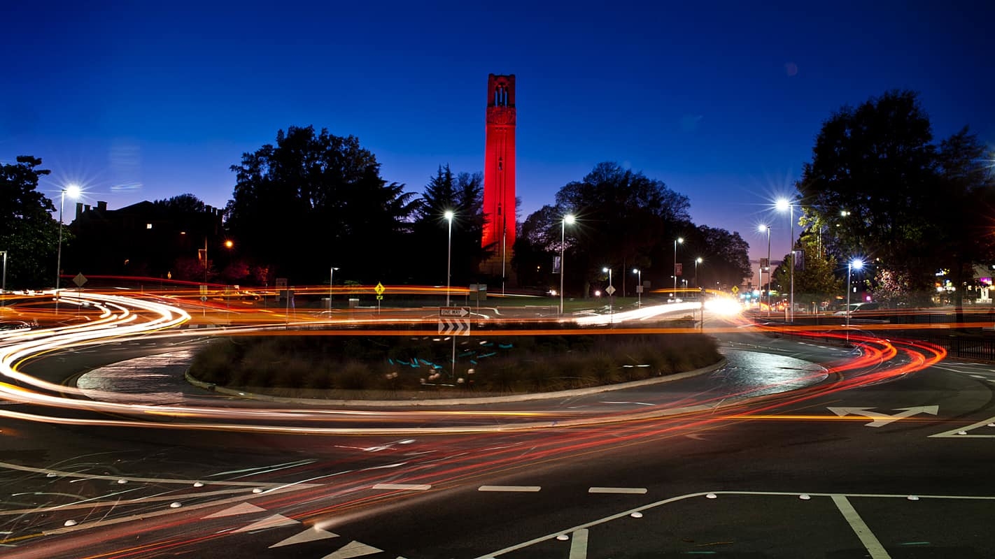 NC State Belltower lit red at night with the Hillsborough Street traffic circle in the foreground