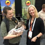 Professor Erin Baker standing next to one of her students who is carrying a baby kangaroo