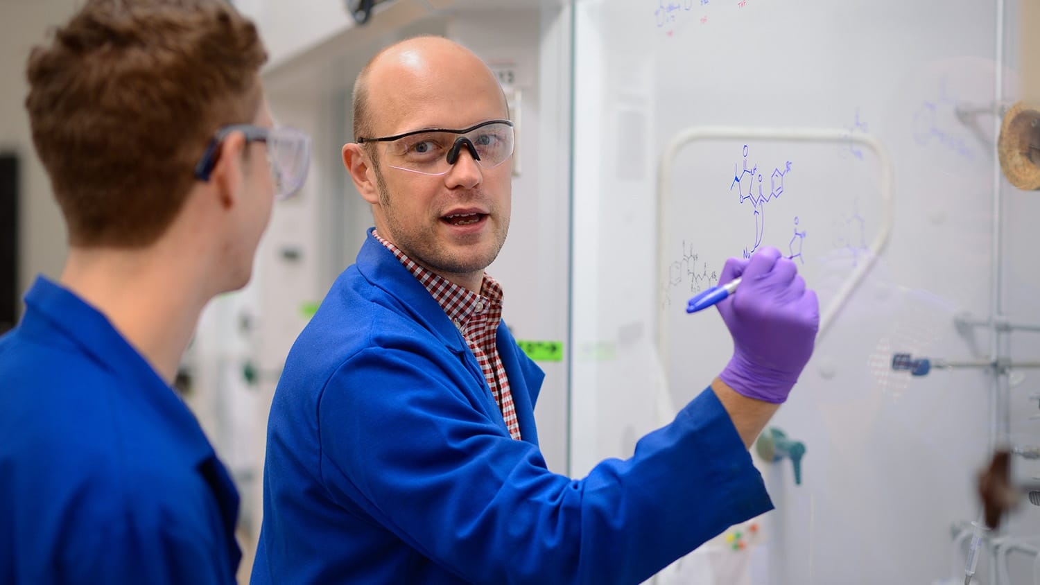 Chemistry professor Joshua Pierce writes on a whiteboard while talking to a student
