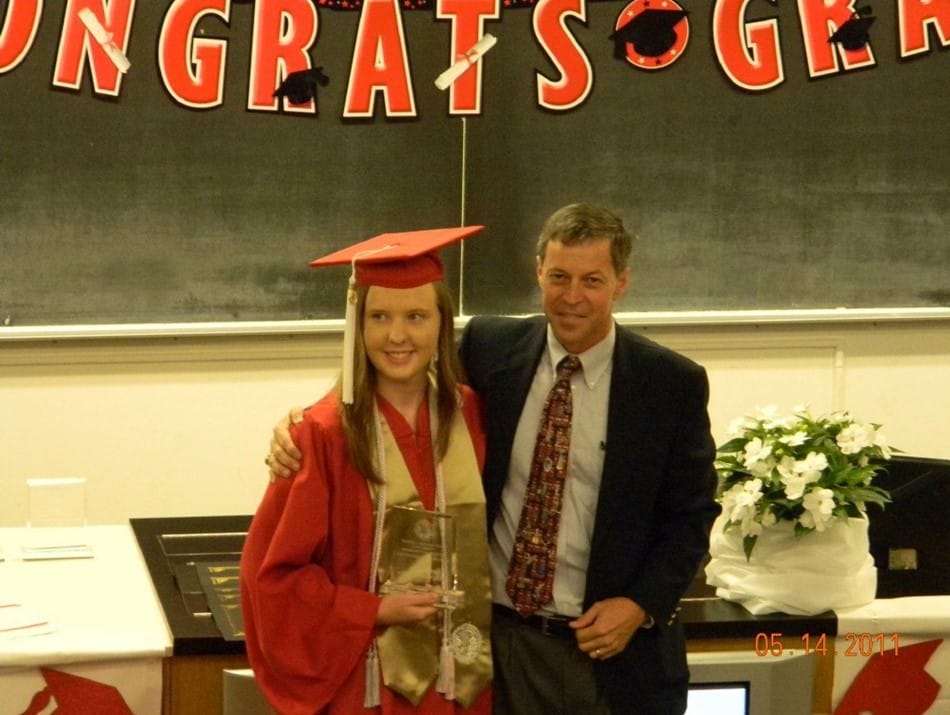 A young student in cap and gown standing beside her advising professor on graduation day