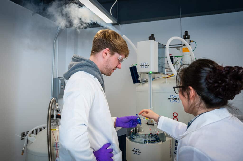 two scientists wearing white gowns working in the lab