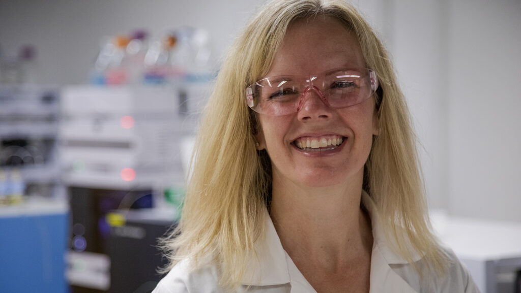 Dr. Erin Baker wearing goggles and a lab coat smiling