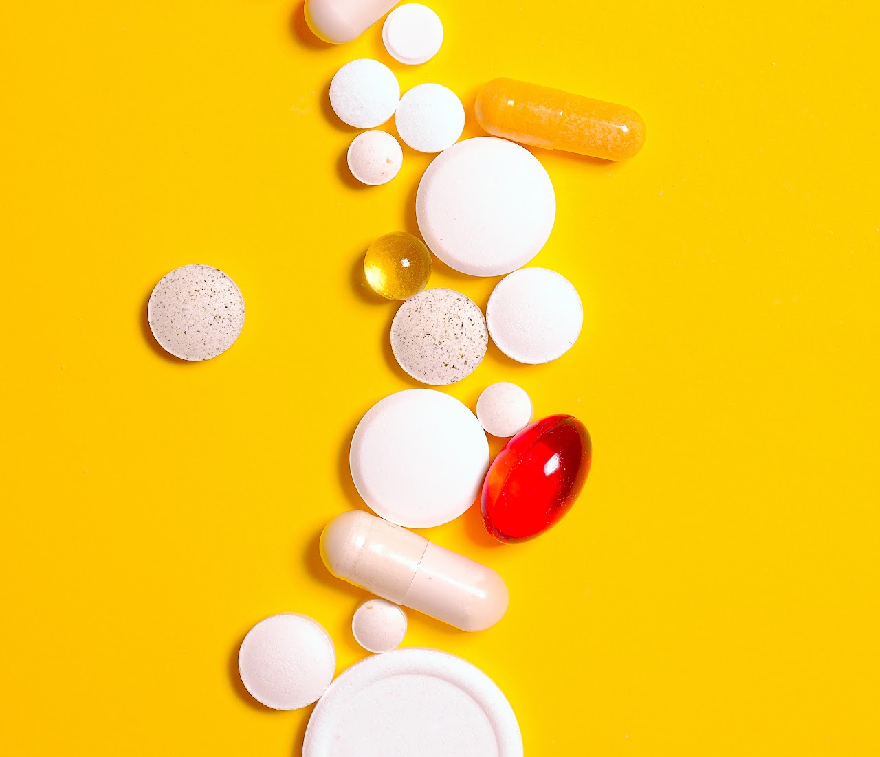Medication pills of different forms and colors scattered on a yellow background