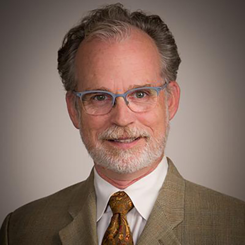 The image represents the headshot of Professor Eric Anslyn from the University of Texas at Austin wearing a suit with a brown tie