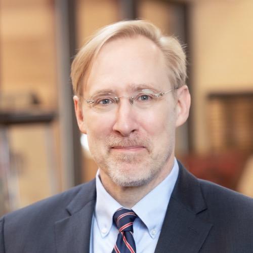 The image represents the headshot of Professor Walter Fast wearing a suit and a tie. Behind him the background is blurred