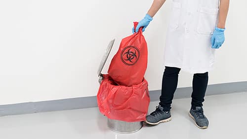 Scientist wearing blue gloves holding red bag with bioharzard sign