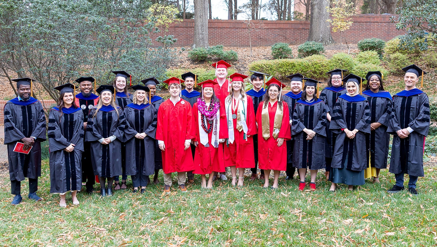 A group photo of recently graduated students wearing caps and gwns standing outdoors on the loan